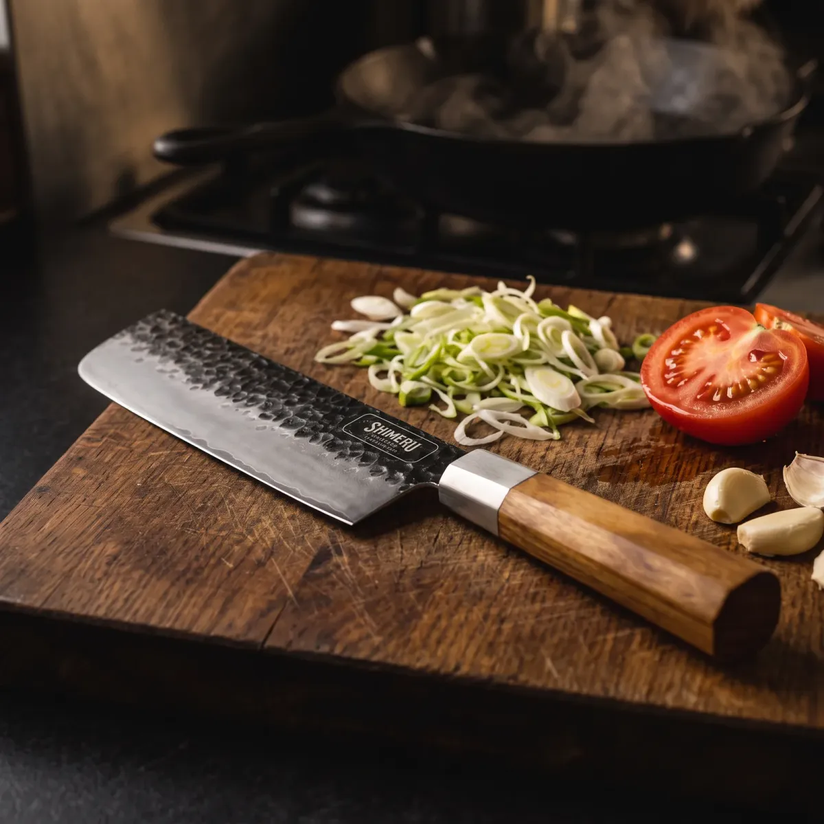 Chitose 7" Nakiri Knife on an oak board with spring onions, tomato and garlic