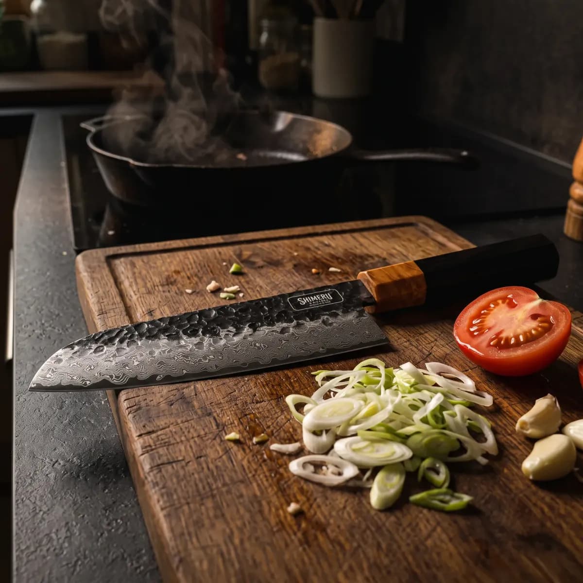 Dark Grain 7" Damascus Steel Santoku Knife on an oak board with spring onions, tomato and garlic